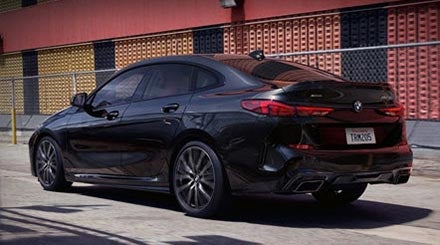 Un BMW Serie 2 Gran Coupé negro zafiro metalizado pasa por delante de un edificio rojo y amarillo.