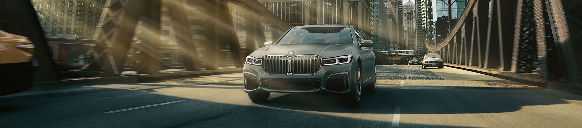 Un BMW Serie 7 Gris Bernina Efecto Ámbar conduciendo por el puente de la ciudad.