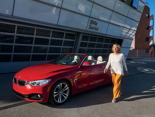 Un cliente pasa junto a un BMW Serie 4 aparcado frente a un centro de servicio BMW.