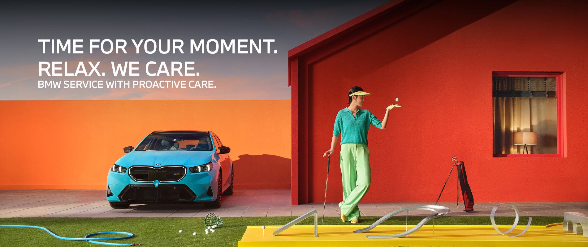 Un BMW M5 Touring aparcado frente a una casa, con una persona que sostiene un palo de golf junto a un green improvisado en el césped.