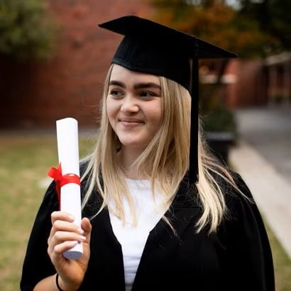 Una mujer sonriente sostiene su título vestida con toga y birrete de graduación.